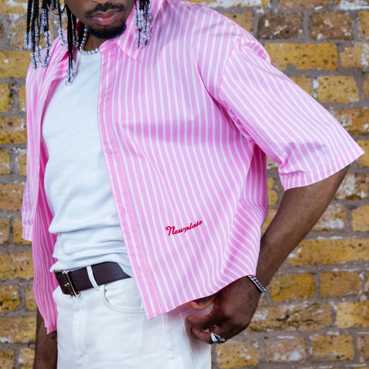 Person wearing a pink striped shirt with a brand logo against a brick wall.